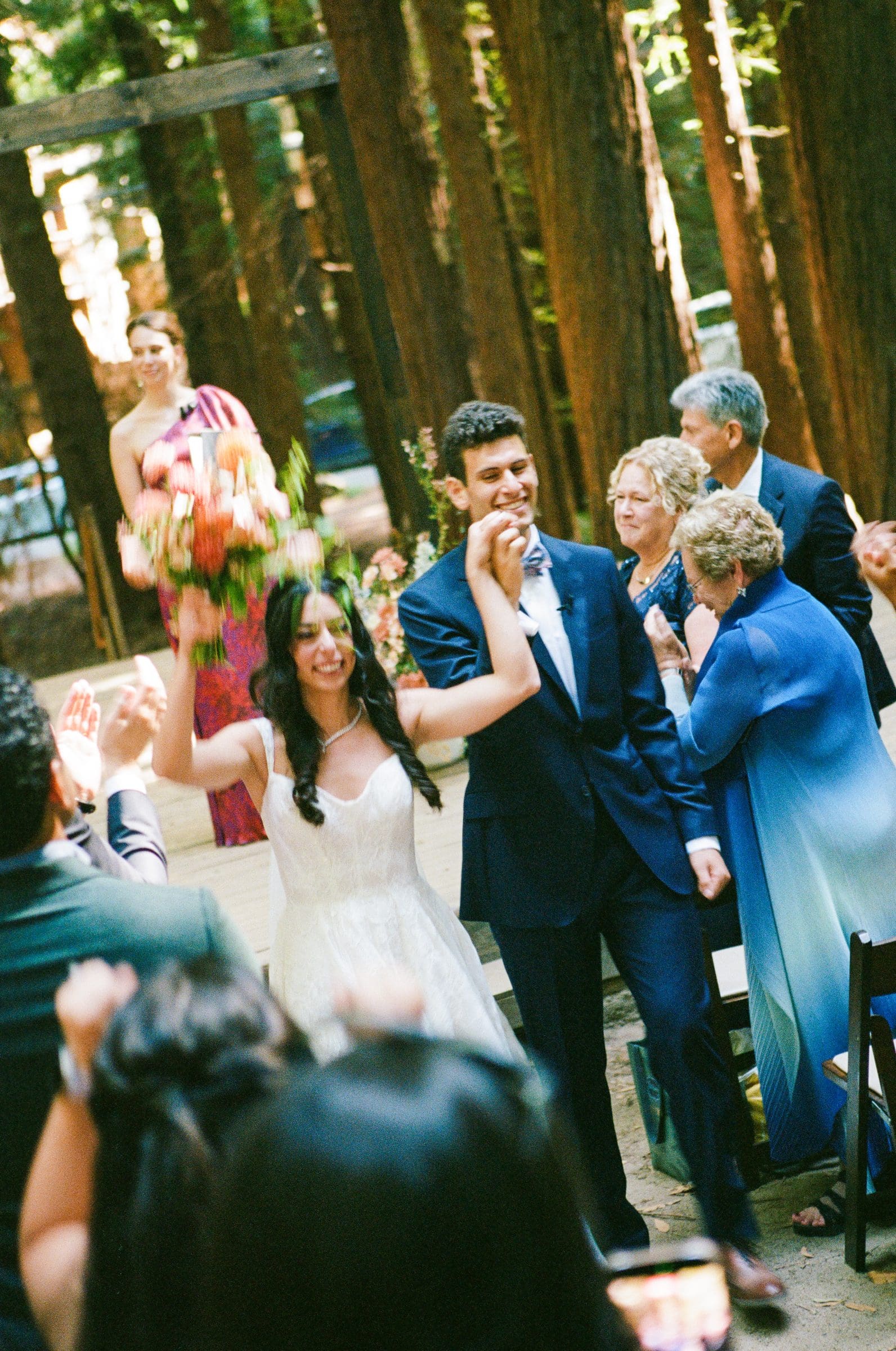 Adam and Lala walking back up the aisle as guests cheer, on film