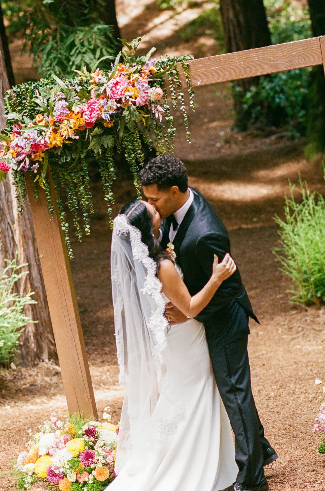 First kiss under the floral arch in the redwoods, on film