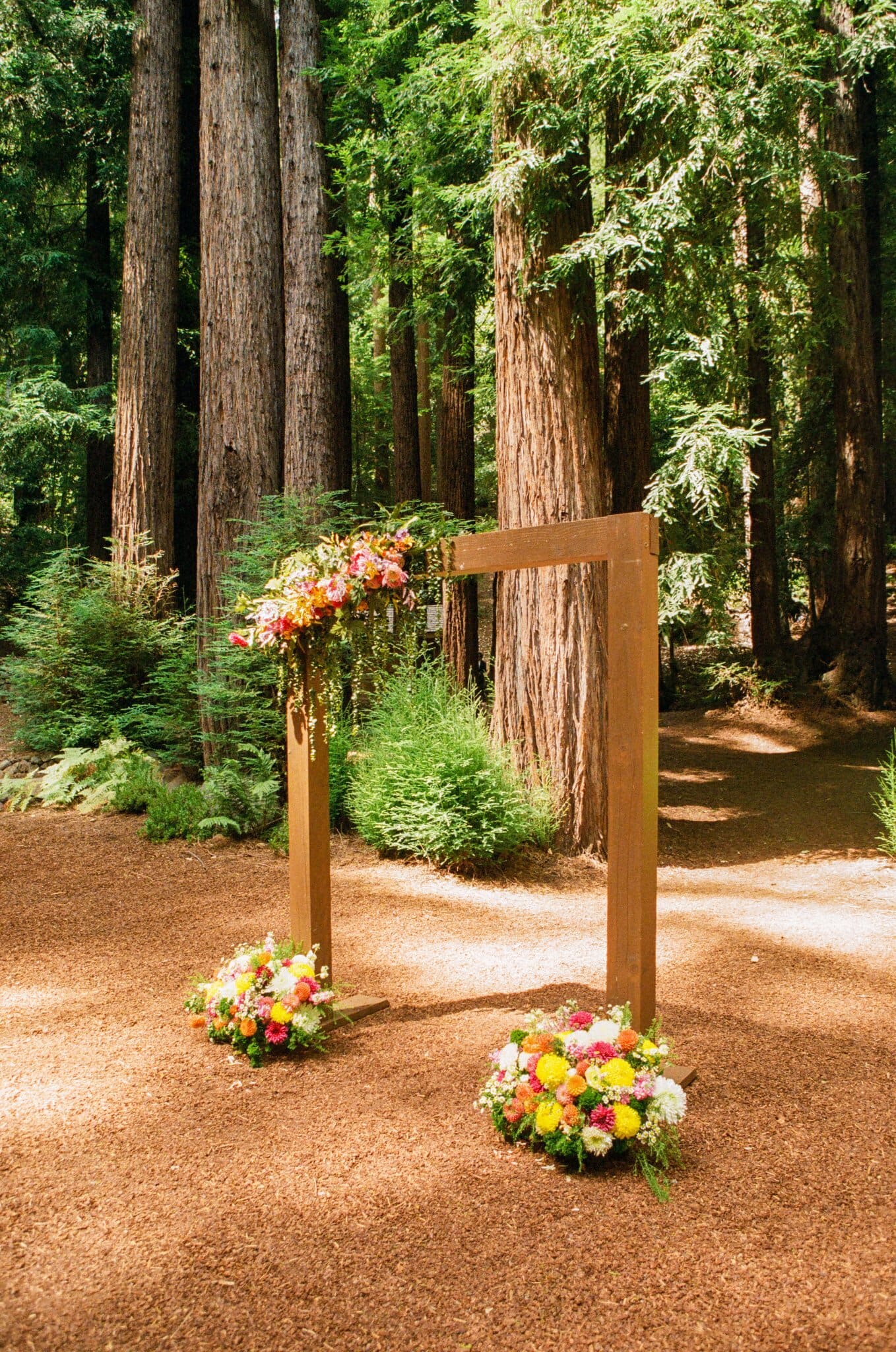 Wooden ceremony arch with bright florals in the redwood grove at Waterfall Lodge & Retreat