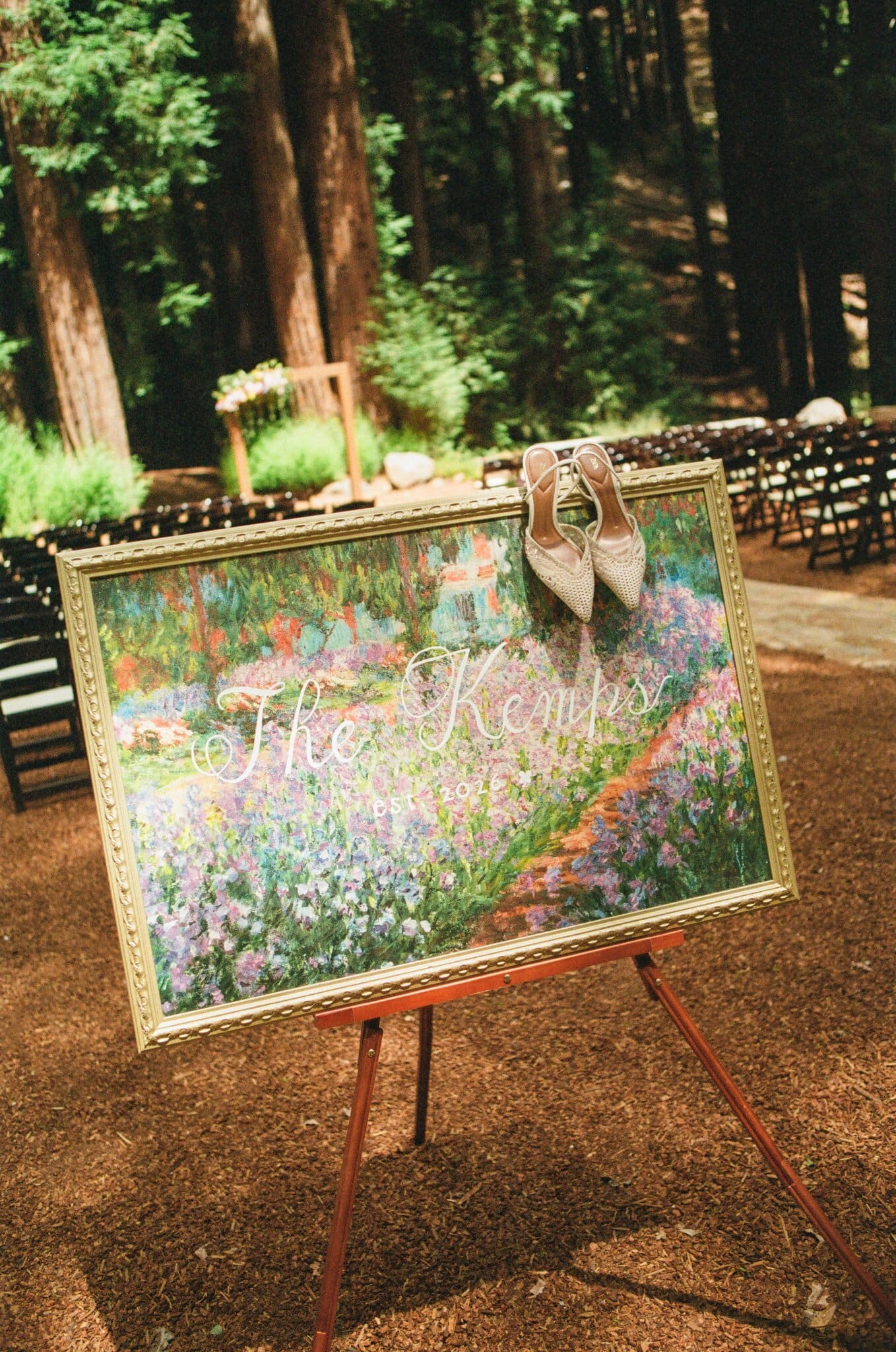 Painted welcome sign on an easel with the bride's shoes in the redwoods