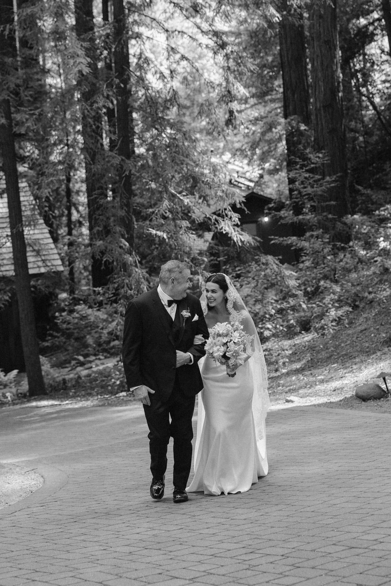 Sofia's dad walking her toward the ceremony through the redwoods, black and white
