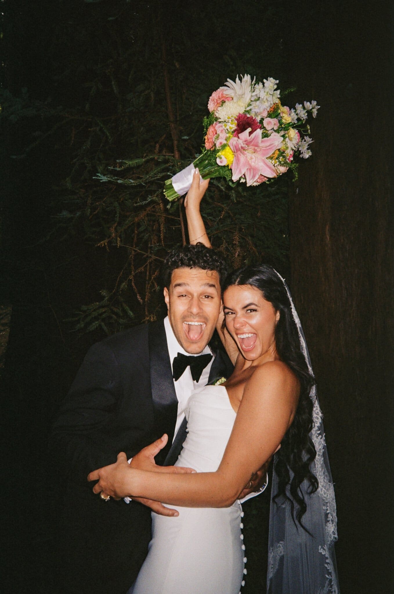 Sofia and Devin celebrating with the bouquet raised, flash on film