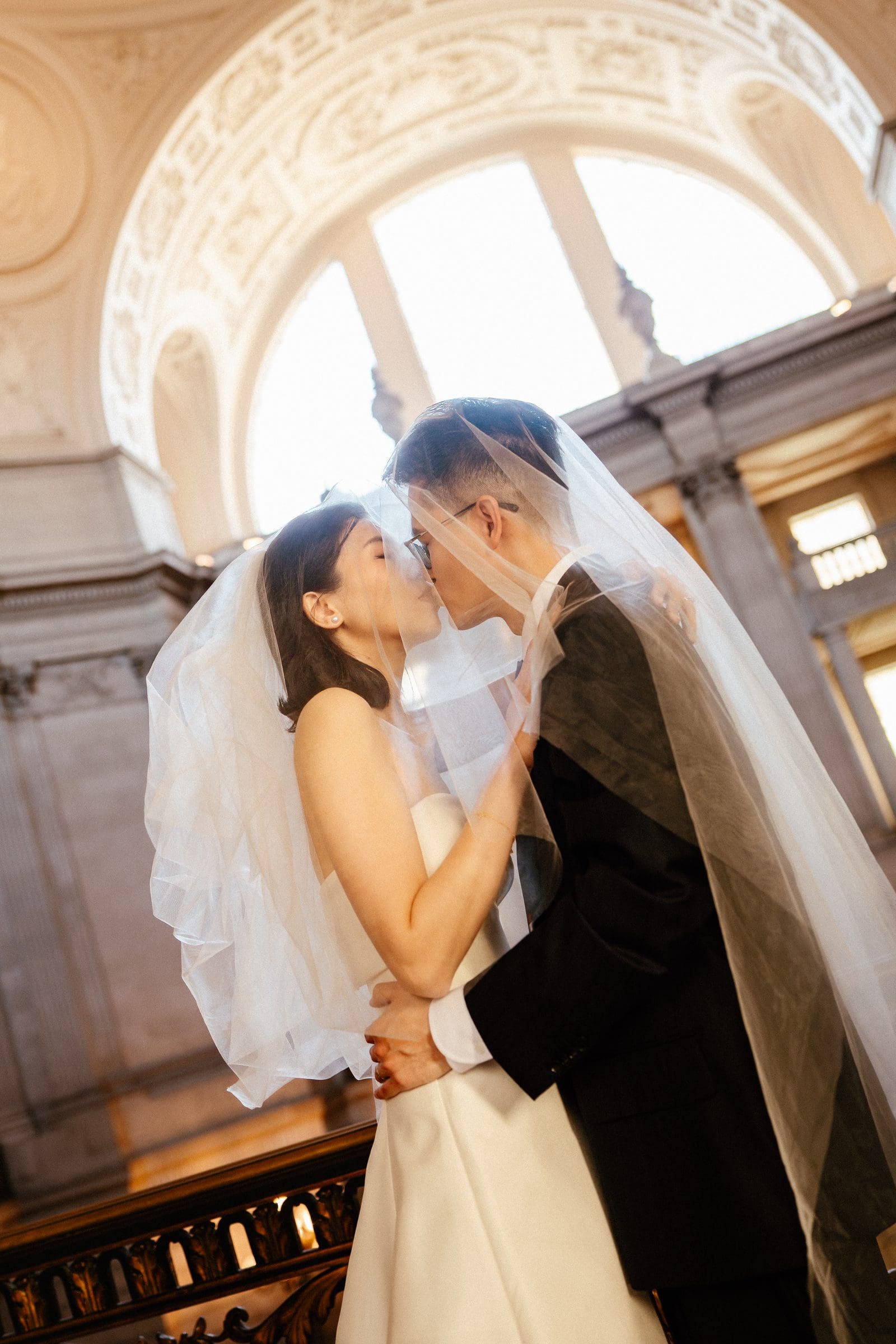 Ting and Hsiang kissing beneath the arched windows of City Hall