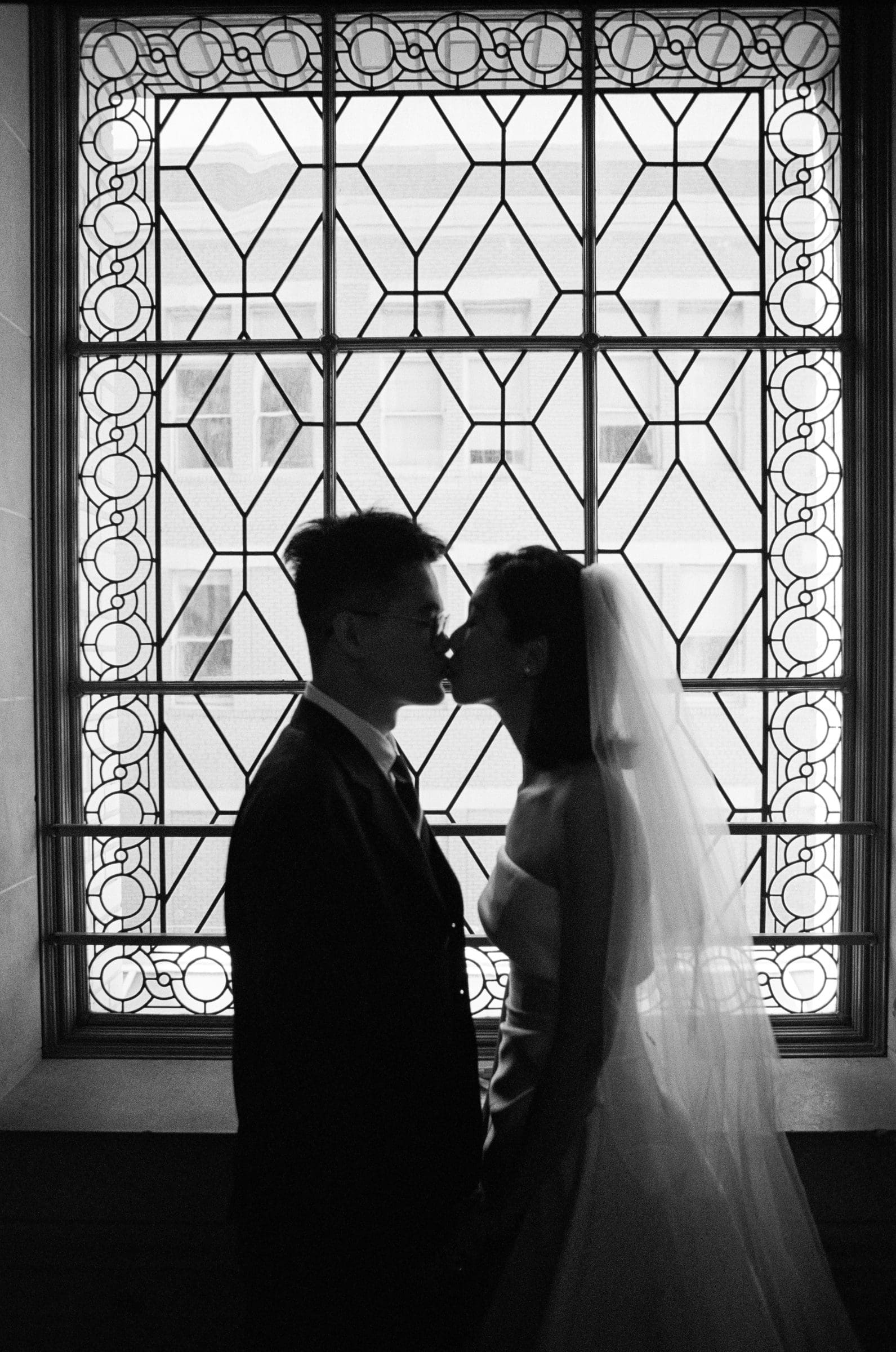 Hsiang and Ting kissing in front of a City Hall window, black and white film