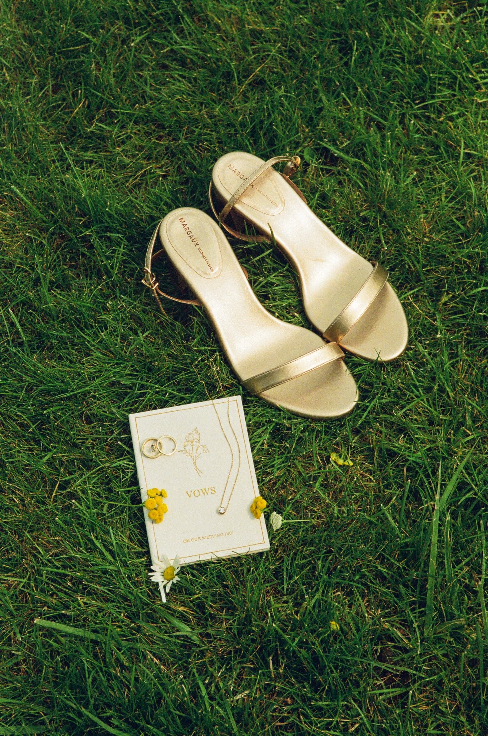 Isabelle's gold wedding shoes and vow book on the grass, on film