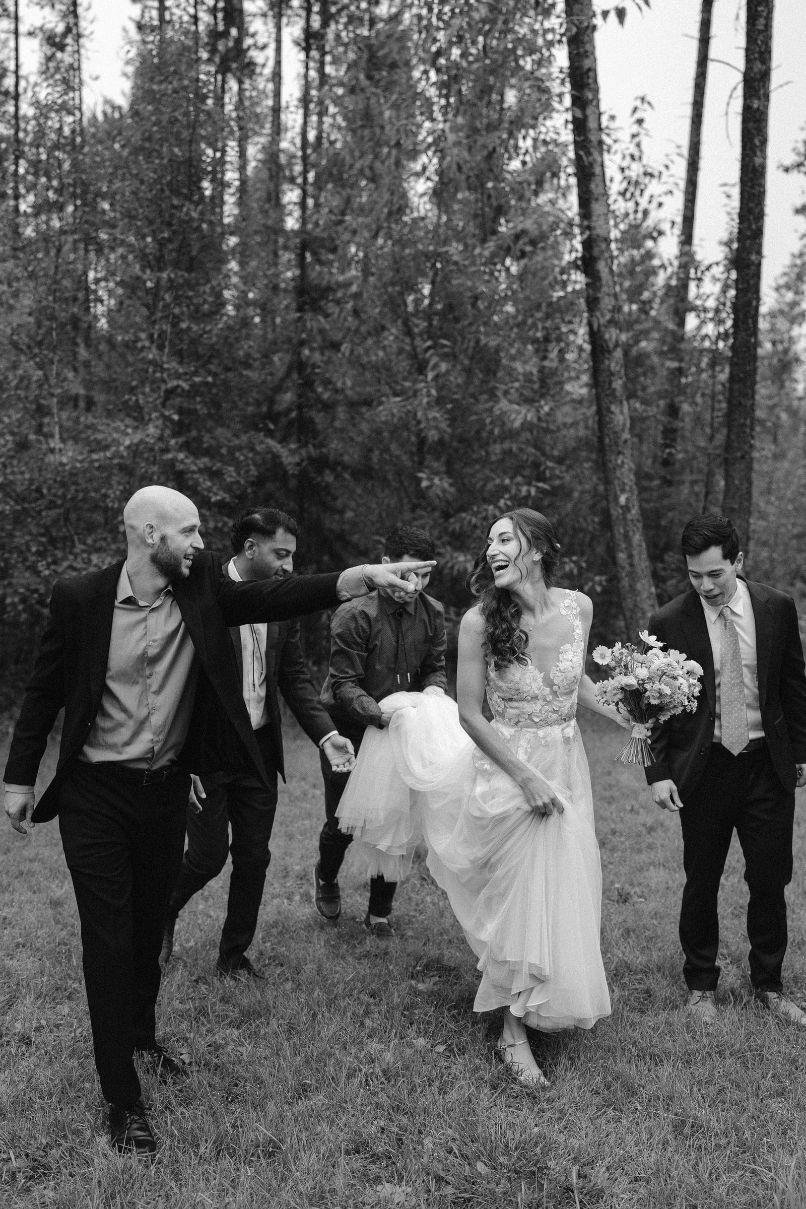 Raj and Isabelle walking with the wedding party through the forest, black and white