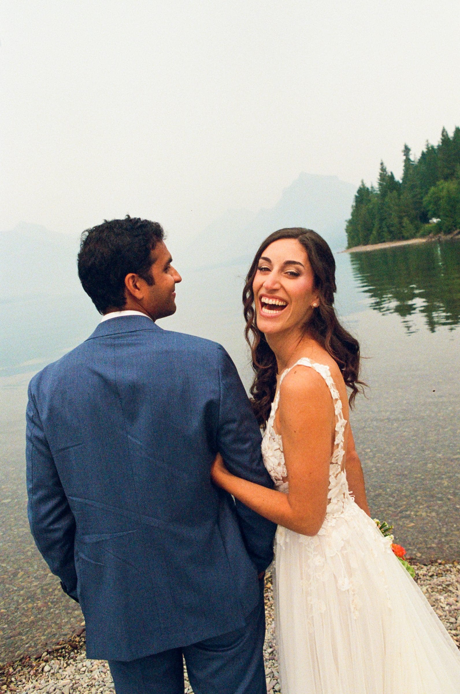 Raj and Isabelle laughing together on the shore of Lake McDonald, on film