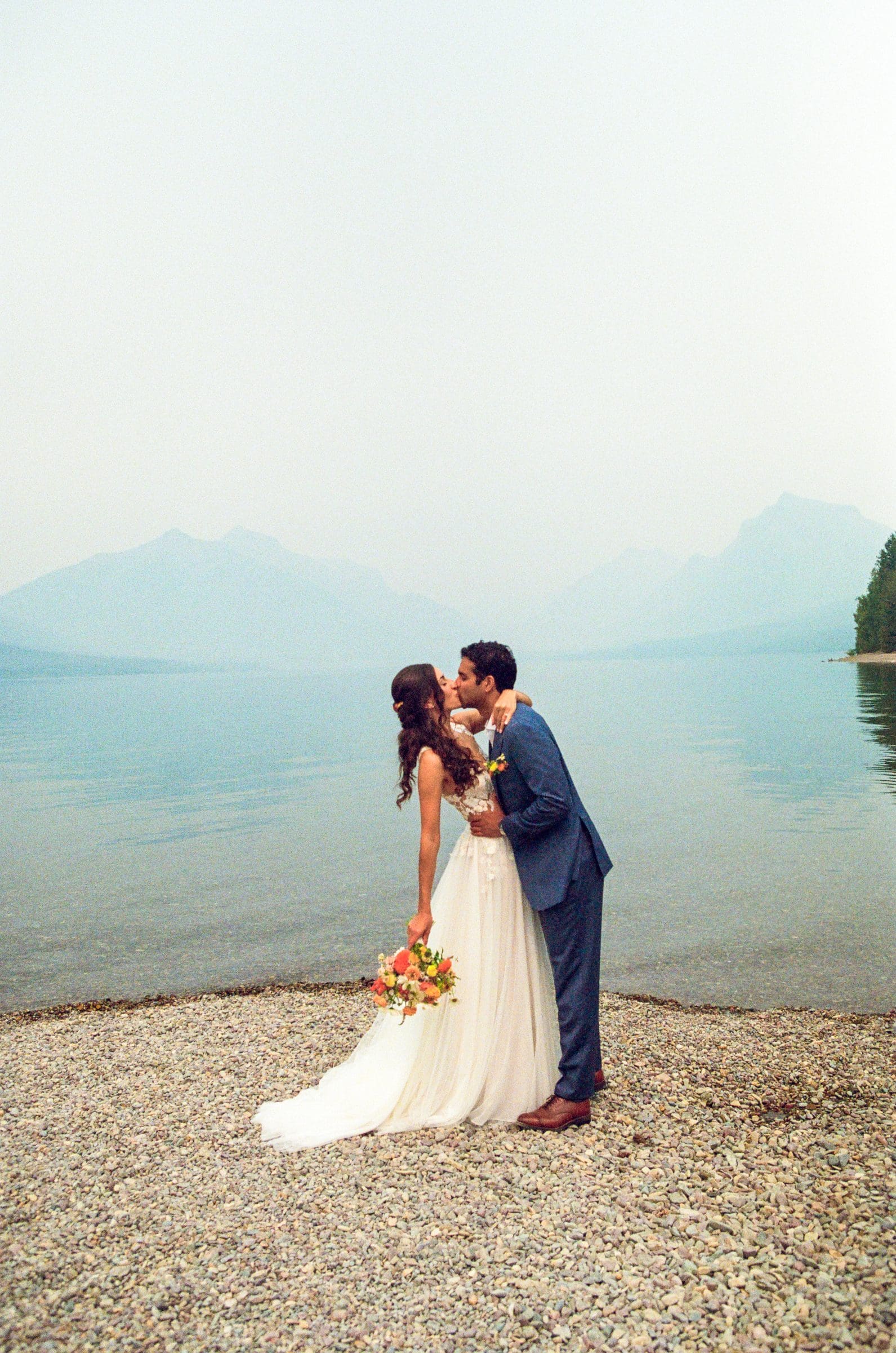 Raj and Isabelle kissing on the Lake McDonald shoreline with the mountains behind, on film